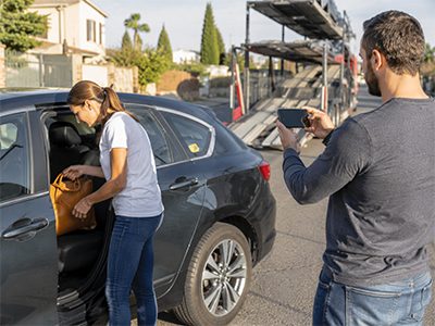 Driver loading a sedan onto an open auto transport carrier